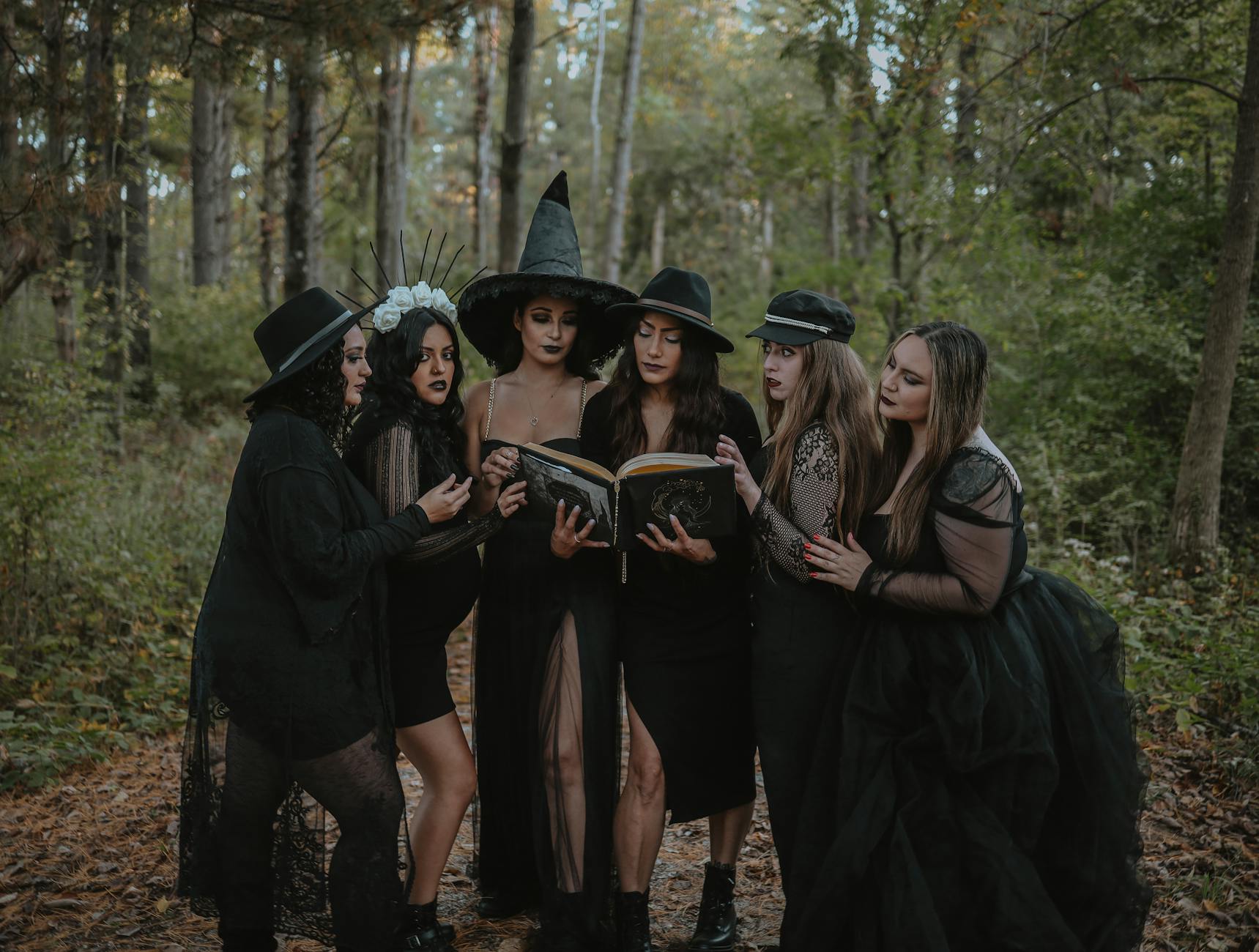 group of women dressed as witch coven reading spell book in forest